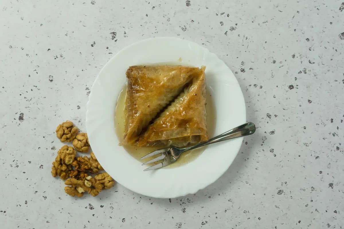 A single slice of baklava served on a white plate with a fork