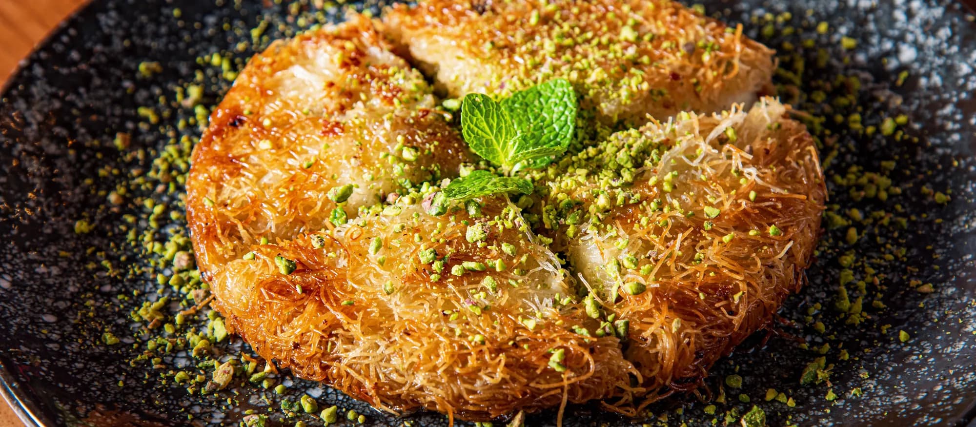 A whole knafeh baked golden in its pan and finished with crushed pistachio