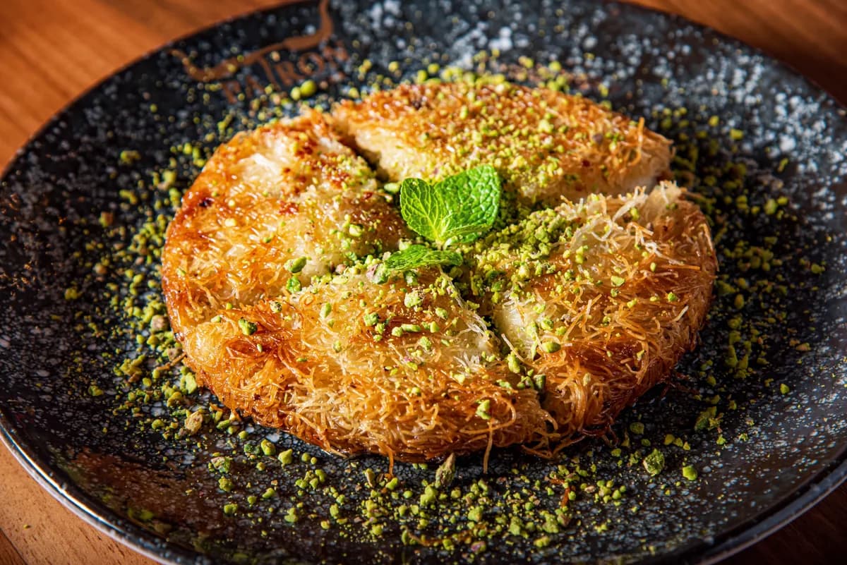 A whole knafeh baked golden in its pan and finished with crushed pistachio