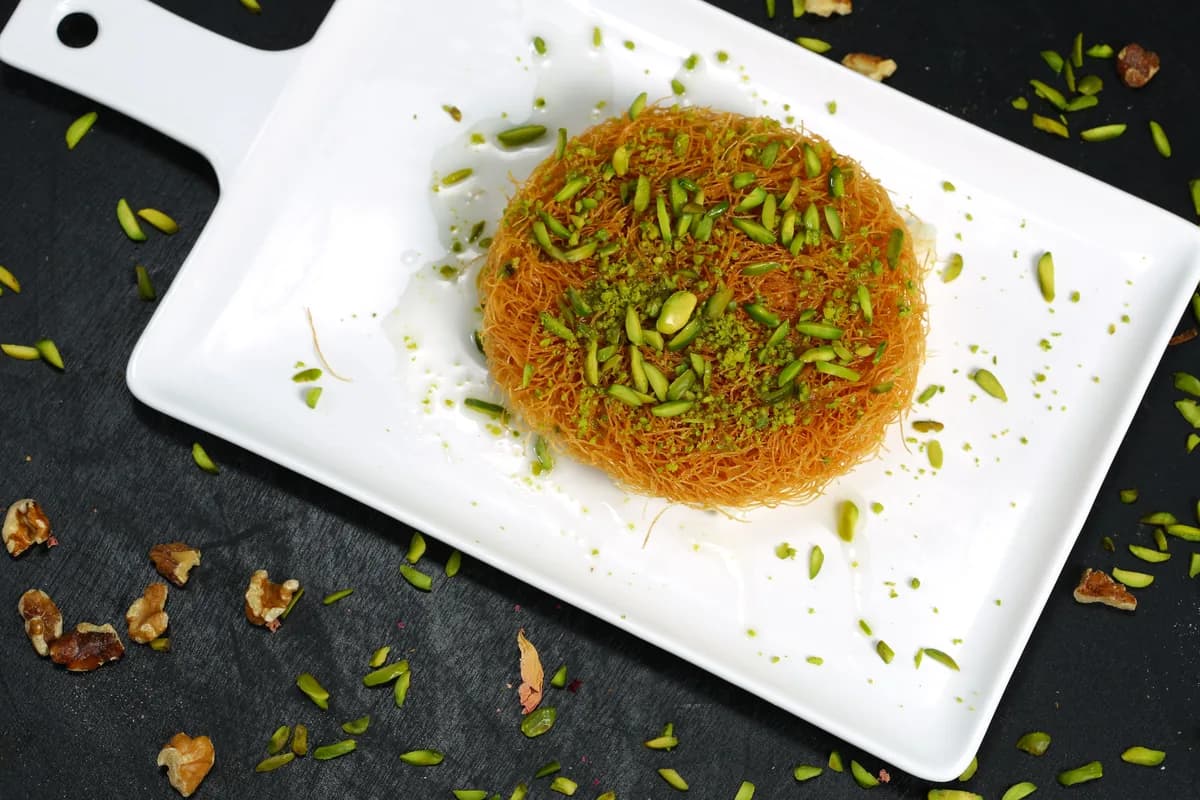 A round of knafeh finished with pistachio, plated for serving