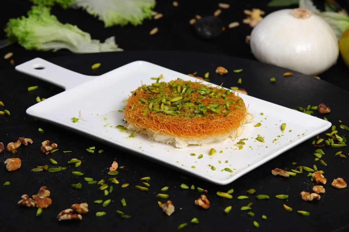 A slice of knafeh topped with crushed pistachio on a white plate
