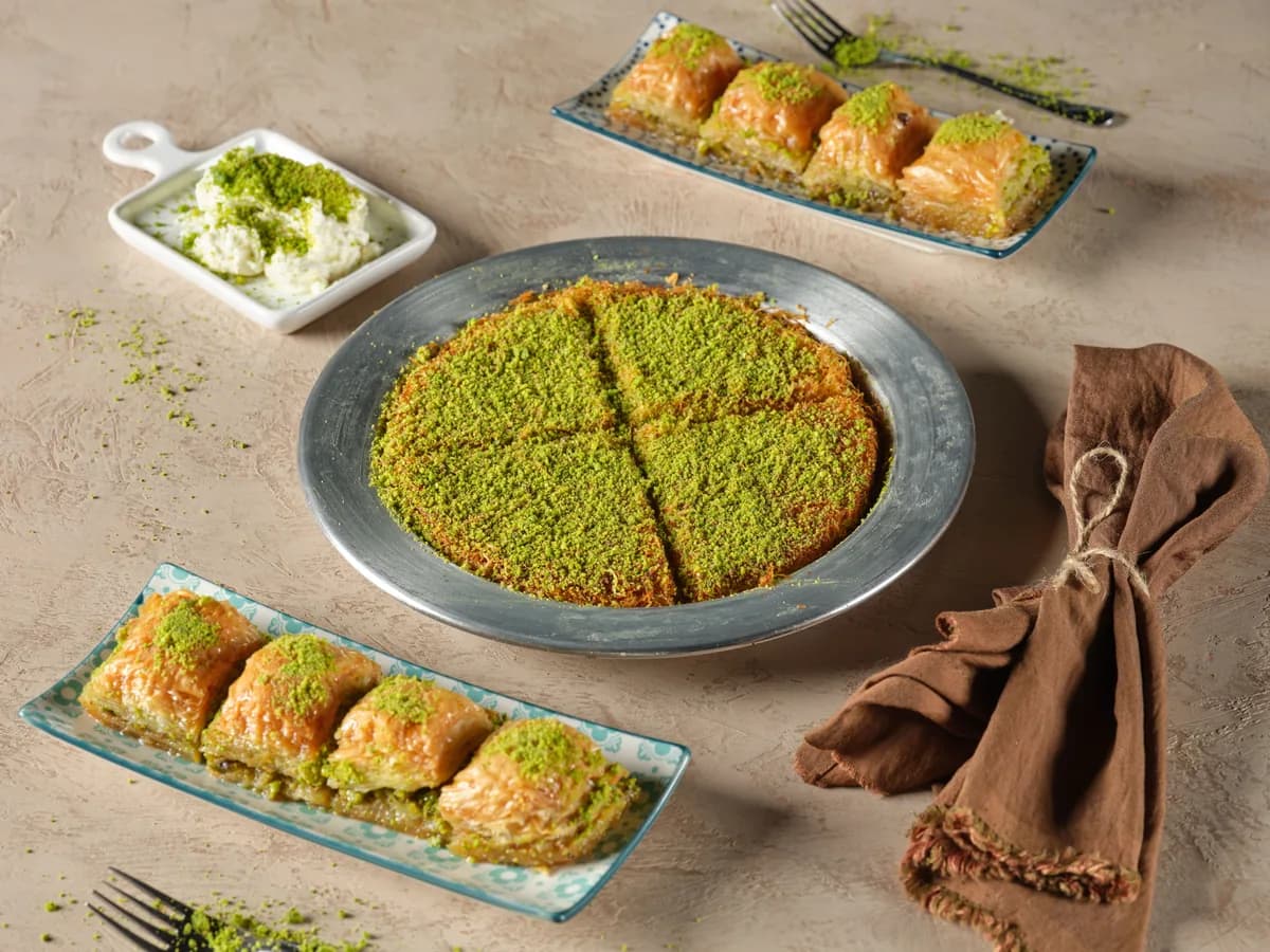 A wedge of pistachio knafeh served on a metal tray alongside baklava