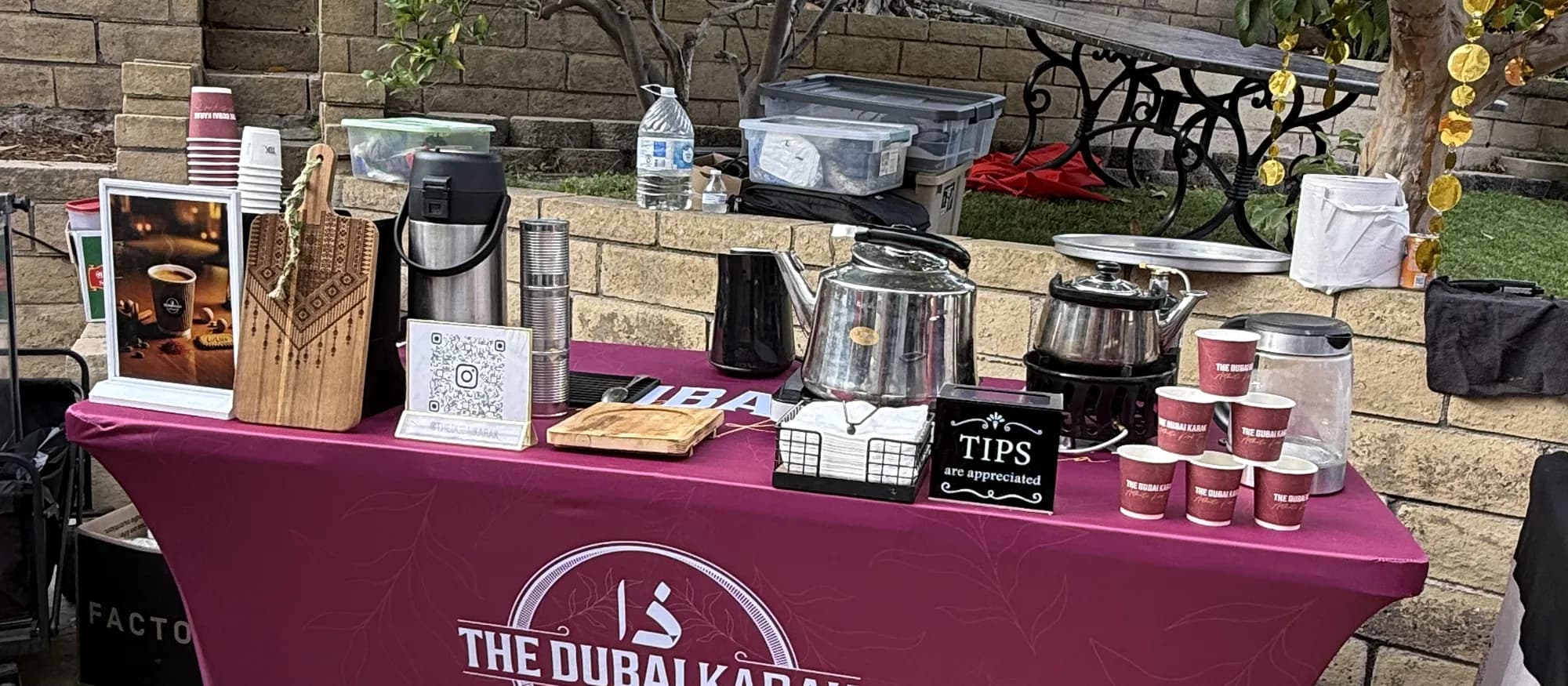 The Dubai Karak maroon branded table set up outdoors with urns, cups and serving equipment